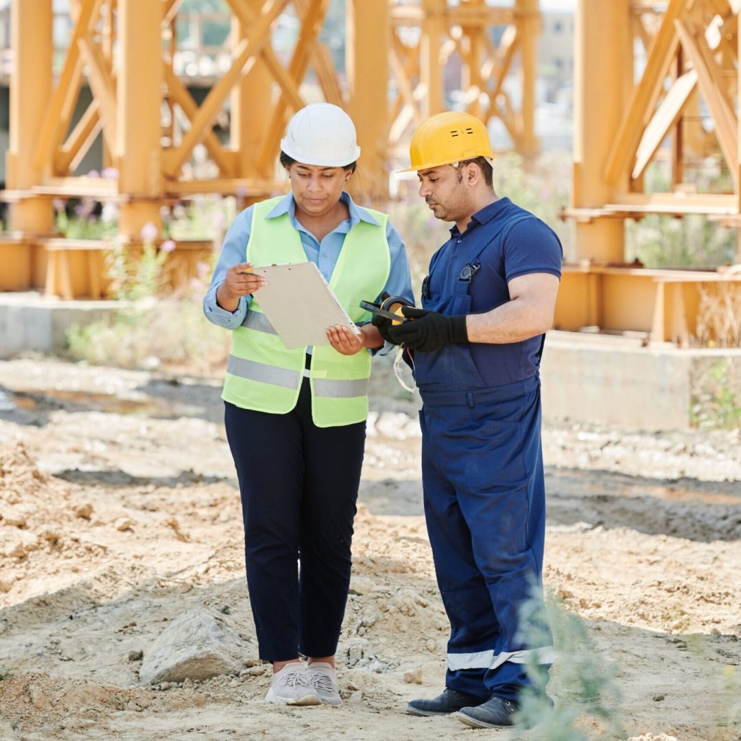 Two construction workers on site, discussing project plans with safety gear and hard hats.